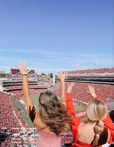 two girls at a football game reaching up to catch the ball