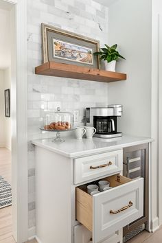 a kitchen with white cabinets and wooden shelves above the counter, has an open drawer underneath it