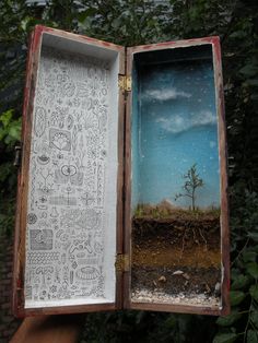 an open book with pictures in it sitting on a table next to some trees and bushes