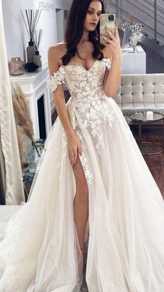 a woman taking a selfie while wearing a wedding dress with thigh high slits