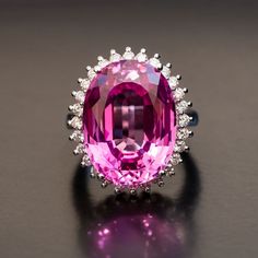 The feminine appeal of our Fantine Pink Sapphire Diamond Ring is undeniable. From the one carat of dainty, individually-set diamonds along the edge of the setting, to the incredible facet-rich depths of the substantial 25 carat center stone, this pink sapphire cocktail ring is made to be admired. With every subtle movement of your hand, this diamond-accented piece glitters brilliantly, showcasing the rich, saturated pink hue at the heart. Supported by a modern basket-style setting in smooth whit Pink Sapphire Diamond Ring, Ring Day, Sapphire Cocktail Ring, Red Sapphire, Pink Sapphire Ring, Natural Diamond Ring, Sapphire Diamond Ring, Fine Jewelry Collection, Sapphire Diamond