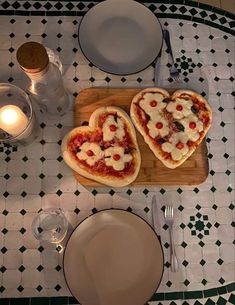 two heart shaped pizzas sitting on top of a wooden cutting board next to a plate