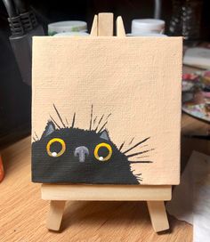 a black cat painted on an easel with yellow eyes