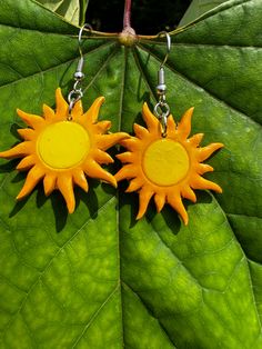 two yellow sunflowers are hanging from earrings on a green leaf