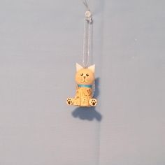 a cat ornament hanging from a chain on a blue surface with a white background