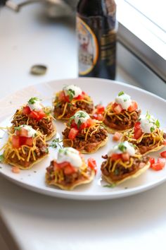 some taco cups are sitting on a white plate next to a bottle of beer