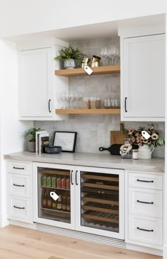 a kitchen with white cabinets and shelves filled with wine glasses on top of the counter