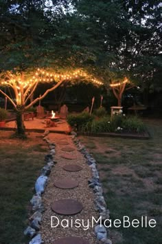 a stone path in the middle of a yard with lights strung over it and trees