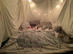 an unmade bed with lights strung from the ceiling