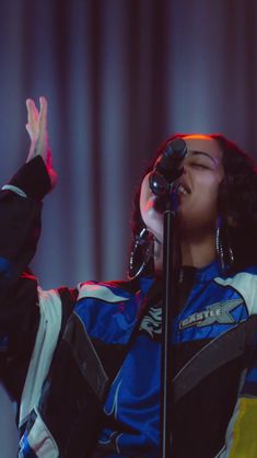 a woman singing into a microphone while holding her hands up in the air with both hands