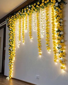 yellow and white flowers are hanging from the wall with lights on it's sides