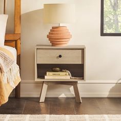 a nightstand with books and a lamp on it in a bedroom next to a bed