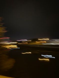 blurry photograph of city lights at night from across the street, with trees in foreground