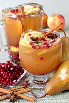 two glasses filled with apple cider next to pears and cinnamon sticks