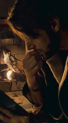 a man sitting in front of a fire with his hands on his face and looking at something