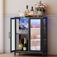 a liquor cabinet with bottles and glasses on top, next to a vase filled with flowers