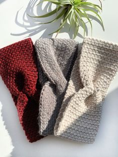 three knitted scarves sitting next to a plant