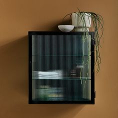 a wall mounted shelf with a plant and bowl on top, against a tan wall