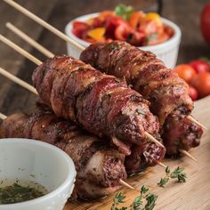 several skewers of meat and vegetables on a cutting board with dipping sauces