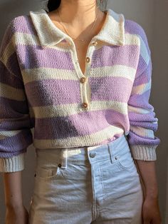 a woman standing in front of a wall wearing a purple and white striped sweater with buttons