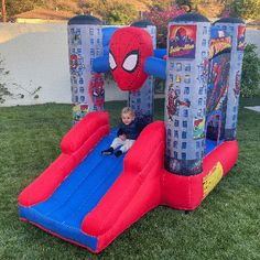 a little boy is playing in an inflatable spiderman bounce house on the lawn