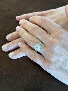 two hands holding each other on top of a wooden table with a diamond ring in the middle