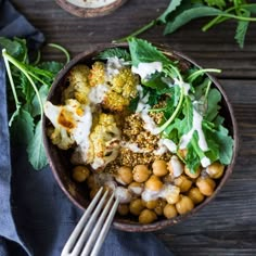 a bowl filled with broccoli, chickpeas and other food on top of a wooden table