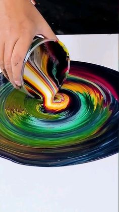 a person pouring liquid onto a plate with colorful swirls on it and a hand holding a can