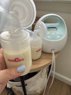 a person holding a baby bottle next to an electric breast pump on a small table