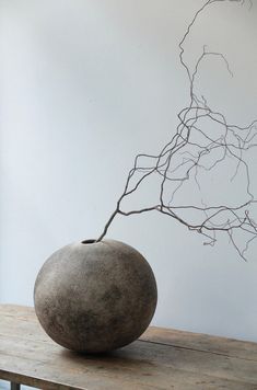 a stone vase sitting on top of a wooden table next to a tree branch sculpture