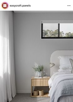 a white bed sitting under a window next to a nightstand with a lamp on it