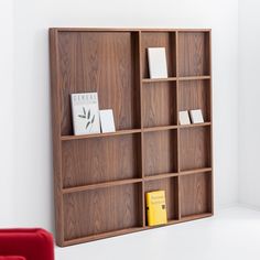 a book shelf with several books on it in a white room next to a red chair