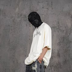 a man wearing a black mask standing in front of a concrete wall with his back to the camera