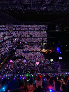 a large group of people standing in front of a stage filled with lights and balloons