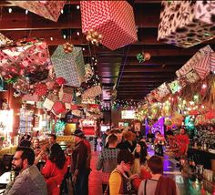 many people are sitting at tables in a restaurant with lights hanging from the ceiling and decorations on the walls