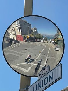 a mirror that is on the side of a pole with a street sign in front of it