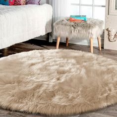 a bedroom with a white bed and furry rugs on the wooden floor next to a window