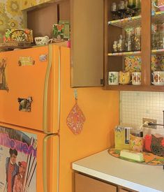 an orange refrigerator in a kitchen with pictures on the door and shelves above it that are full of magnets