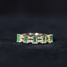 an emerald and diamond ring sitting on top of a black surface with gold trimming