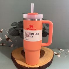 an orange travel mug sitting on top of a piece of wood with a straw in it