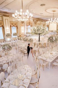 a bride and groom standing in the middle of a banquet hall with tables set for formal function