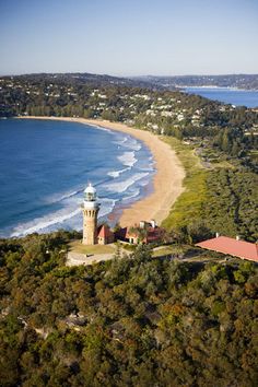 an aerial view of a lighthouse on the coast with trees and water in the background