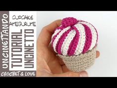 a crocheted cupcake with pink, white and gray stripes is in someone's hand