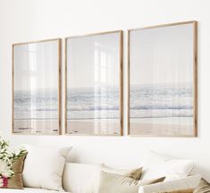 three framed pictures hang on the wall above a white couch with pillows and flowers in front of it