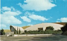 an old photo of a building in the middle of a road with trees and bushes around it