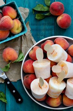 a bowl filled with sliced up peaches next to a knife and some other fruit