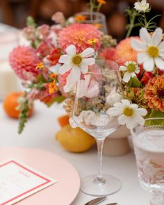 an arrangement of flowers in vases and wine glasses on a table with place settings