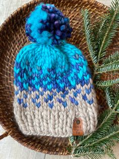 a knitted hat sitting on top of a basket next to a pine tree branch