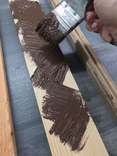 someone using a brush to paint wood planks with dark brown paint on it,