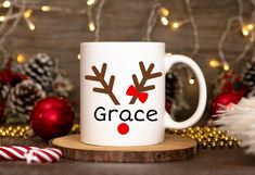 a white coffee mug with reindeer antlers on it sitting in front of christmas decorations